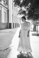 elegante mezzo età donna nel un' bianca Vintage ▾ vestito contro il sfondo di storico edifici nel il mattina leggero foto