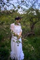 bellissimo donna nel bianca Vintage ▾ vestito con treno nel primavera giardino a tramonto foto