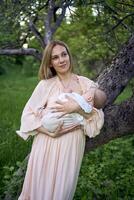 bellissimo madre è l'allattamento al seno sua bambino ragazza nel il giardino foto