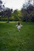 un' poco ragazza con lungo capelli corre attraverso il giardino con un' cestino pieno di fiori foto