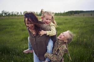 un' madre rotoli sua figlie su sua Indietro, giocando cavallo, baci e abbracci foto