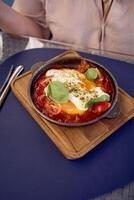 medio dimensioni donna nel pesca fuzz vestito mangiare Shakshuka nel moderno ristorante foto