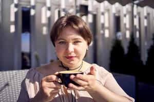 un' medio dimensioni donna nel pesca fuzz vestito con tazza di caffè nel caffè negozio nel mattina leggero foto