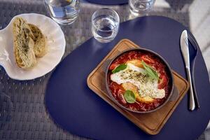 medio dimensioni donna nel pesca fuzz vestito mangiare Shakshuka nel moderno ristorante foto