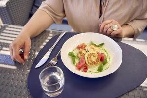 un' medio dimensioni donna nel pesca fuzz vestito mangiare Villetta formaggio Pancakes con salmone e spinaci nel moderno ristorante foto