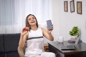 attraente bellissimo donna nel bianca attrezzatura visualizzazione Mela e mobile schermo su telecamera foto