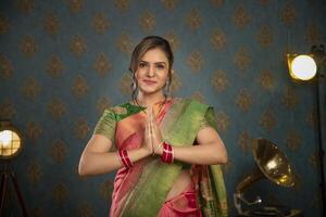 un' dolce signora nel tradizionale abbigliamento durante Diwali Festival mostrando namaste gesto nel davanti di il telecamera foto