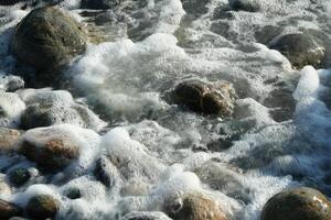 schiuma di un' onda nel il mare, ciottoli, acqua foto