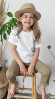 vuoto unisex tela bambino piccolo maglietta modello, colore bianca, ragazza modello seduta su un' sgabello indossare cachi pantaloni e un' cappello foto