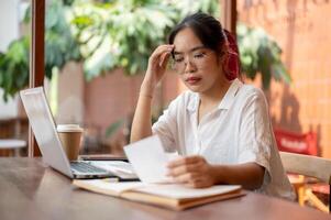 un' serio, stressato asiatico donna è Lavorando remoto a un' caffè negozio, controllo fatture. foto