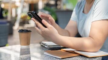 un' ritagliata tiro di un asiatico donna utilizzando sua smartphone mentre seduta a un all'aperto tavolo a un' bar. foto