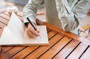 un' uomo scrittura nel il suo taccuino, annotare giù idee, o conservazione un' diario mentre seduta nel un' bar. foto