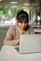 un' giovane asiatico femmina Università alunno Lavorando remoto a un' mensa, Lavorando su sua il computer portatile computer. foto