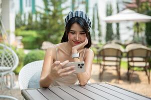 un attraente asiatico donna Guardando video su sua smartphone mentre seduta nel un' bellissimo giardino. foto