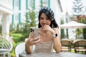 un' donna ride a sua Telefono e gode chat con sua amici in linea mentre rilassante nel un' giardino. foto