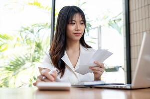 un' femmina contabile è controllo fatture e ricevute, Lavorando su attività commerciale finanziario dati su sua il computer portatile foto