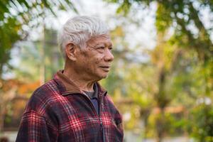 ritratto di un anziano uomo sorridente e guardare lontano mentre in piedi nel un' giardino. spazio per testo. concetto di anziano persone e assistenza sanitaria foto