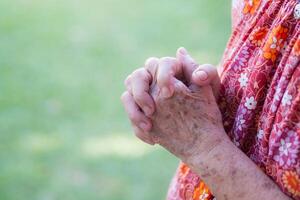 avvicinamento di mani anziano donna Iscritto insieme per pregare mentre in piedi nel un' giardino. spazio per testo. concetto di anziano persone e religione foto
