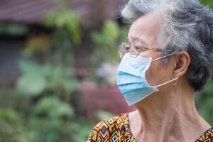 lato Visualizza di un' anziano donna indossare un' viso maschera e guardare lontano mentre in piedi nel un' giardino. maschera per proteggere covid19, coronavirus, batteri, eccetera. concetto di anziano persone e assistenza sanitaria foto