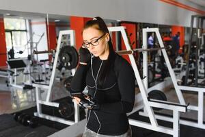 ritratto di giovane sportiva con smartphone ascoltando per musica nel palestra. foto