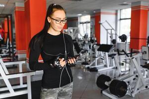 ritratto di giovane sportiva con smartphone ascoltando per musica nel Palestra foto