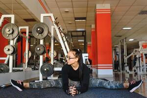 bella ragazza fare allungamento esercizi su il pavimento a il palestra. foto