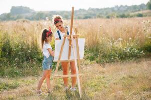 soleggiato natura, mamma e figlia dipingere un' immagine nel un' parco , pittura un' poco bambino, bambino creatività. La madre di giorno. foto