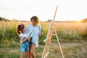 madre insegna figlia dipingere nel parco. soleggiato natura, mamma e figlia dipingere un' immagine nel un' parco , pittura un' poco bambino, bambino creatività. La madre di giorno. foto