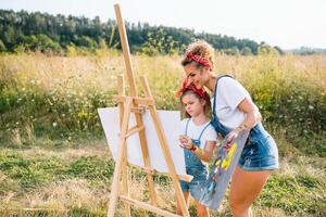 soleggiato natura, mamma e figlia dipingere un' immagine nel un' parco , pittura un' poco bambino, bambino creatività. La madre di giorno. foto