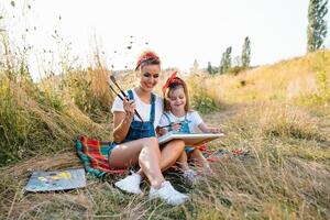 soleggiato natura, mamma e figlia dipingere un' immagine nel un' parco , pittura un' poco bambino, bambino creatività. La madre di giorno. foto