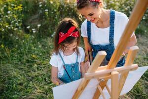 madre insegna figlia dipingere nel parco. soleggiato natura, mamma e figlia dipingere un' immagine nel un' parco , pittura un' poco bambino, bambino creatività. La madre di giorno. foto