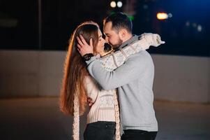 tema ghiaccio pattinando pista e amorevole coppia. incontro giovane, elegante persone cavalcata di mano nel folla su città pattinando pista illuminato di leggero bulbi e luci. ghiaccio pattinando nel inverno per Natale su ghiaccio arena. foto