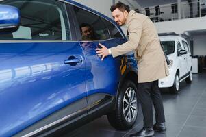 visitare auto concessionaria. bello barbuto uomo è accarezzando il suo nuovo auto e sorridente foto