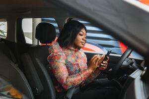 africano americano donna seduta nel auto uso mobile Telefono sms mentre guida pericoloso foto