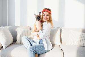 allegro giovane donna Tenere sua grande cucciolo con nero naso e ridendo. interno ritratto di sorridente ragazza in posa con francese bulldog foto