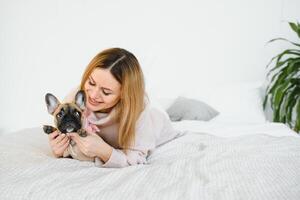 allegro giovane donna Tenere sua grande cucciolo con nero naso e ridendo. interno ritratto di sorridente ragazza in posa con francese bulldog foto