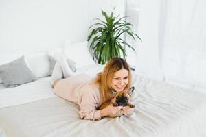 allegro giovane donna Tenere sua grande cucciolo con nero naso e ridendo. interno ritratto di sorridente ragazza in posa con francese bulldog foto