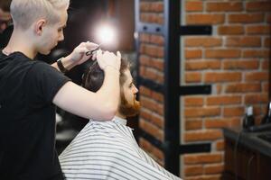 fabbricazione taglio di capelli Guarda Perfetto. giovane barbuto uomo ottenere taglio di capelli di parrucchiere mentre seduta nel sedia a barbiere. foto