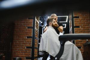 fabbricazione taglio di capelli Guarda Perfetto. giovane barbuto uomo ottenere taglio di capelli di parrucchiere mentre seduta nel sedia a barbiere. foto