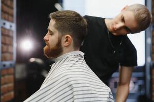 giovane bello barbiere fabbricazione taglio di capelli di attraente barbuto uomo nel barbiere. foto