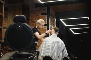 fabbricazione taglio di capelli Guarda Perfetto. giovane barbuto uomo ottenere taglio di capelli di parrucchiere mentre seduta nel sedia a barbiere. foto