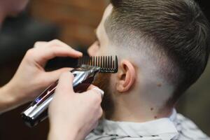 fabbricazione taglio di capelli Guarda Perfetto. giovane barbuto uomo ottenere taglio di capelli di parrucchiere mentre seduta nel sedia a barbiere. foto