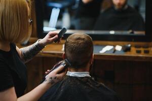 elegante uomo seduta barbiere negozio parrucchiere parrucchiere donna taglio il suo capelli ritratto bello contento giovane barbuto caucasico tipo ottenere di moda taglio di capelli attraente barbiere ragazza Lavorando servendo cliente. foto