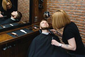 barbiere o parrucchiere concetto. donna parrucchiere tagli barba con forbici. uomo con lungo barba, baffi e elegante capelli. tipo con moderno acconciatura visitare parrucchiere foto