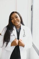 ritratto di sorridente femmina medico indossare bianca cappotto con stetoscopio nel ospedale ufficio. foto
