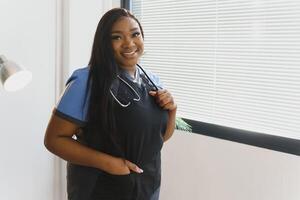 ritratto di bellissimo sorridente femmina africano americano medico in piedi nel medico ufficio. Salute cura concetto, medico assicurazione, copia spazio foto