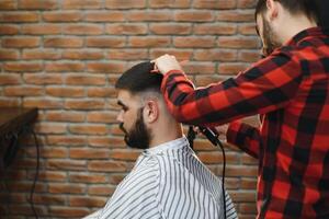 fabbricazione taglio di capelli Guarda Perfetto. giovane barbuto uomo ottenere taglio di capelli di parrucchiere mentre seduta nel sedia a barbiere. foto