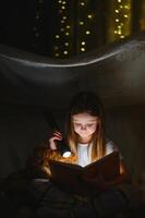 bambino ragazza lettura con libro e torcia elettrica e orsacchiotto orso nel tenda. prima andando per letto foto