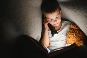 lettura libro e utilizzando torcia elettrica. giovane ragazzo nel casuale Abiti dire bugie giù vicino tenda a sera tempo foto