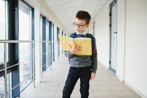 ritratto di contento scuola alunno. inteligente elementare scuola ragazzo bicchieri in piedi nel scuola. poco bambino nel Tenere un' libro. foto